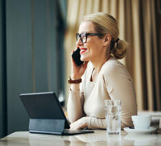 Kvinde taler i telefon med en computer foran sig.