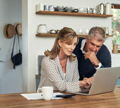 Kvinde viser sin mand en oversigt over pensioner på computer i køkken