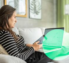 Kvinde med computer og mobil i sofa kigger på sine investeringer